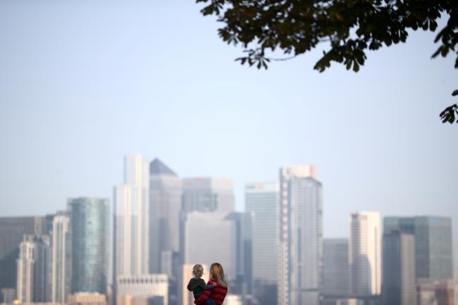 A woman holds a child in front of Canary Wharf skyline, in London, Britain September 14, 2020. REUTERS/Hannah McKay
