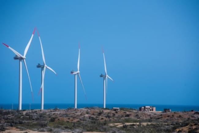 Four big wind turbines loom over a small building in some scrubby open land