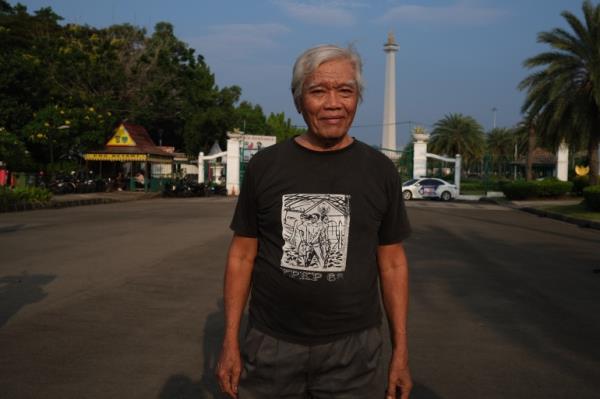 Bejo Untung standing in Jakarta. He is wearing a black T-shirt. MONAS, the natio<em></em>nal monument, is behind him. 
