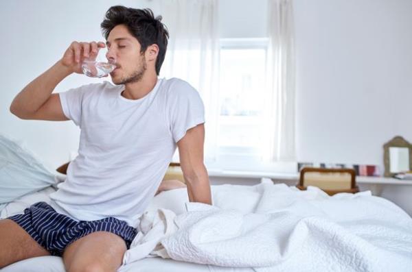 Man sitting in bed drinking water