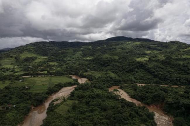 A green hillside with land cleared amid wooded areas and two rivers nearly meeting