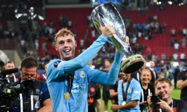 Cole Palmer holds aloft the Uefa Super Cup trophy wearing his medal on his Manchester City kit while being followed by a cameraman at the Georgios Karaiskakis stadium