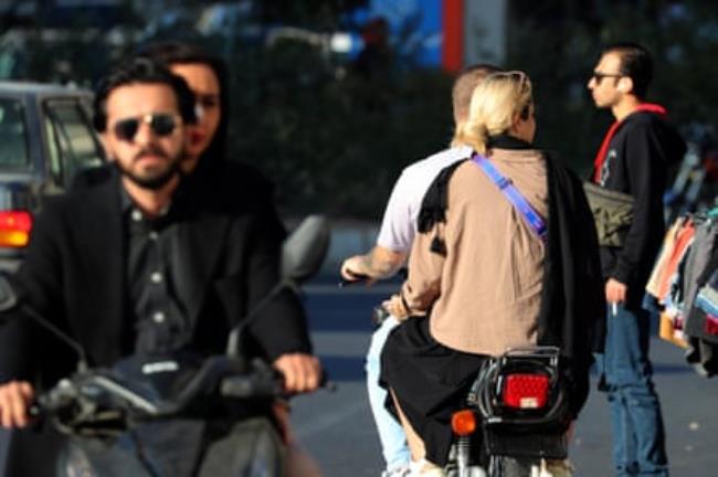 An Iranian woman not wearing headscarf (hijab) on the back of a motorbike in a street in Tehran