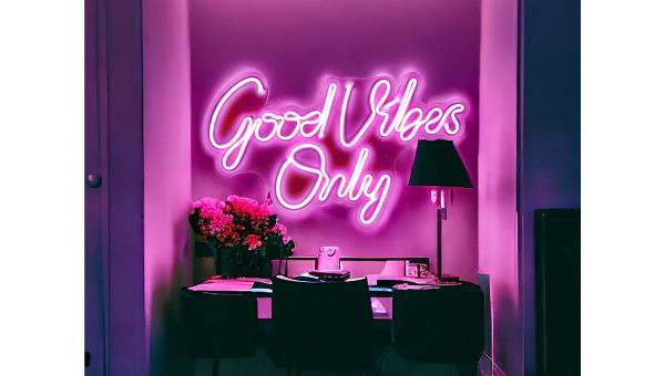 A pink &quot;Good Vibes Only&quot; neon sign on a wall above a desk in a dark room.