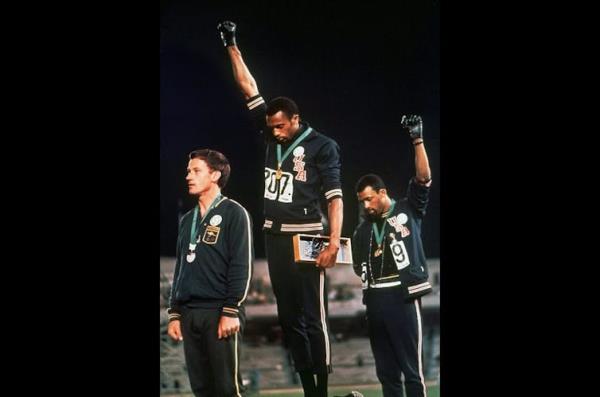 Two black men on a medal podium raise their fists and bow their heads.