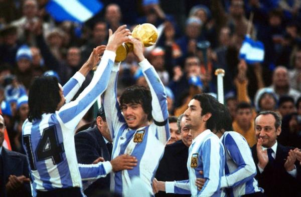 Men in blue-and-white striped soccer jerseys celebrate while holding up a gold trophy.