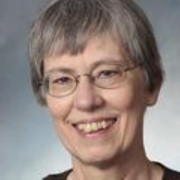 Angela Hoffman, Ph.D., has short gray, straight hair, eye glasses and a black shirt, smiling against a gray background.