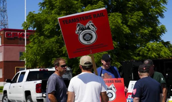 A group of men in t-shirts and ba<em></em>seball caps holding signs that say 'Teamsters Rail'