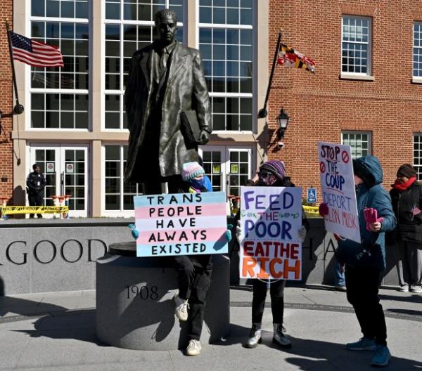 A protesters carry signs under the Thurgood Marshall statue. Protesters rally on President's Day at Lawyers Mall in Annapolis against the policies of President Do<em></em>nald Trump and Elon Musk as part of the natio<em></em>nwide "50501" Movement. (Paul W. Gillespie/Staff)