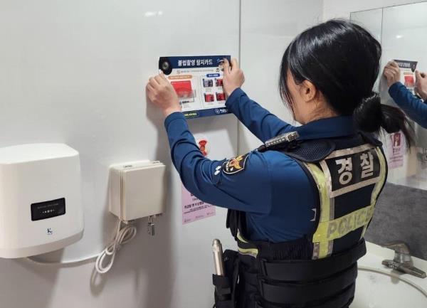 An officer from the Hanam Police Station places a poster a<em></em>bout preventing illegal filming in a public restroom. (Newsis)